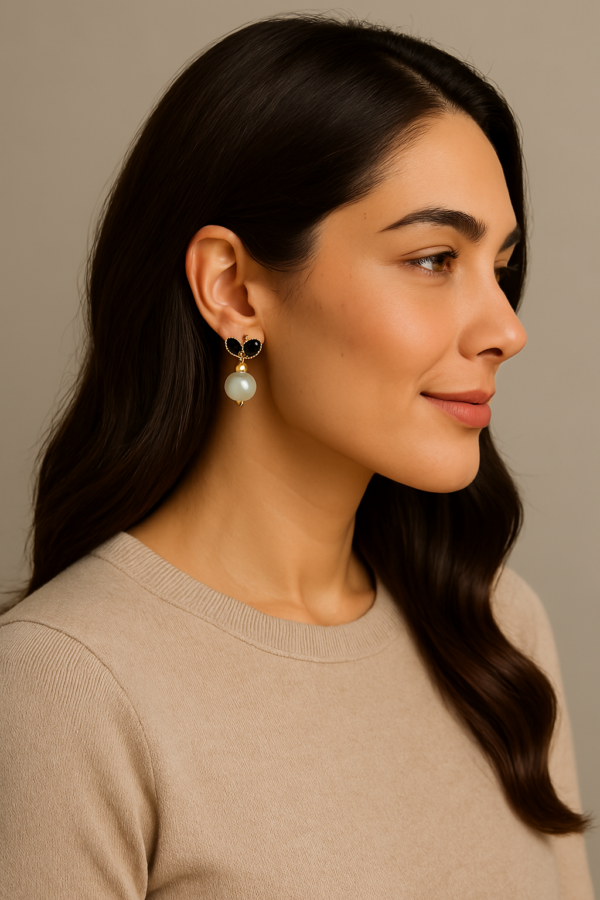 A smiling woman with dark hair and light skin wears butterfly earrings with black enamel details and dangling white pearls.