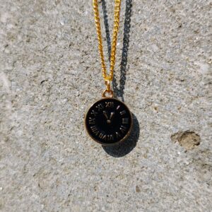 A necklace with a gold-toned chain and a circular clock pendant.