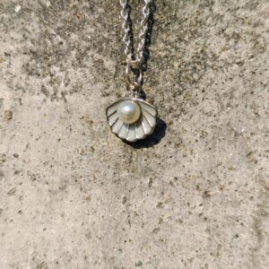 A necklace with a silver chain and a seashell pendant with a pearl.