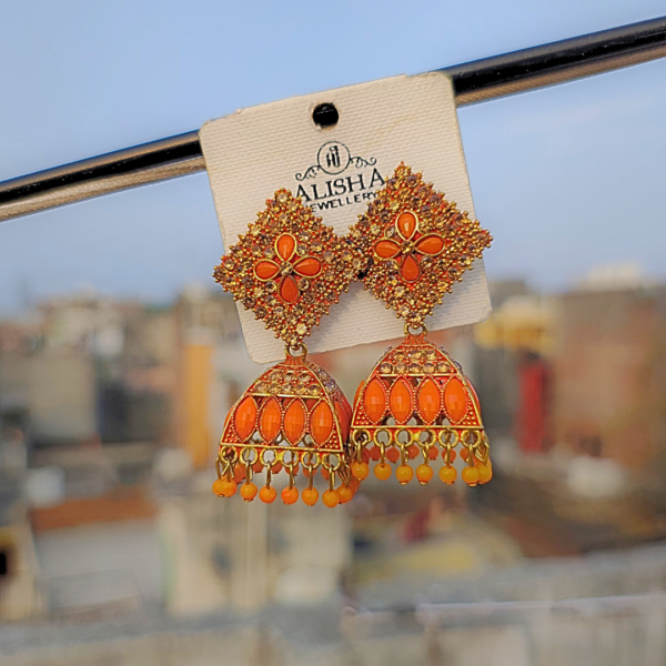 Elegant orange jhumka earrings with intricate detailing, blending traditional and trendy designs, displayed on a jewelry card against a blurred outdoor background.