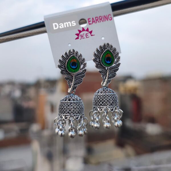 A pair of Peacock Feather Jhumka Earrings with oxidized silver detailing, peacock feather design, and hanging beads, displayed against an outdoor background.