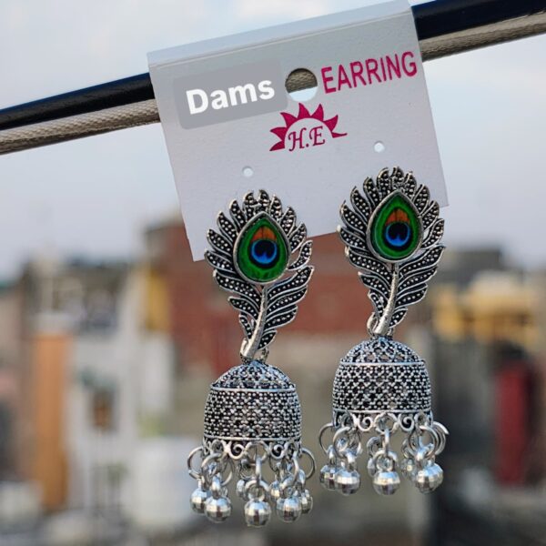 A pair of Peacock Feather Jhumka Earrings with oxidized silver detailing, peacock feather design, and hanging beads, displayed against an outdoor background.