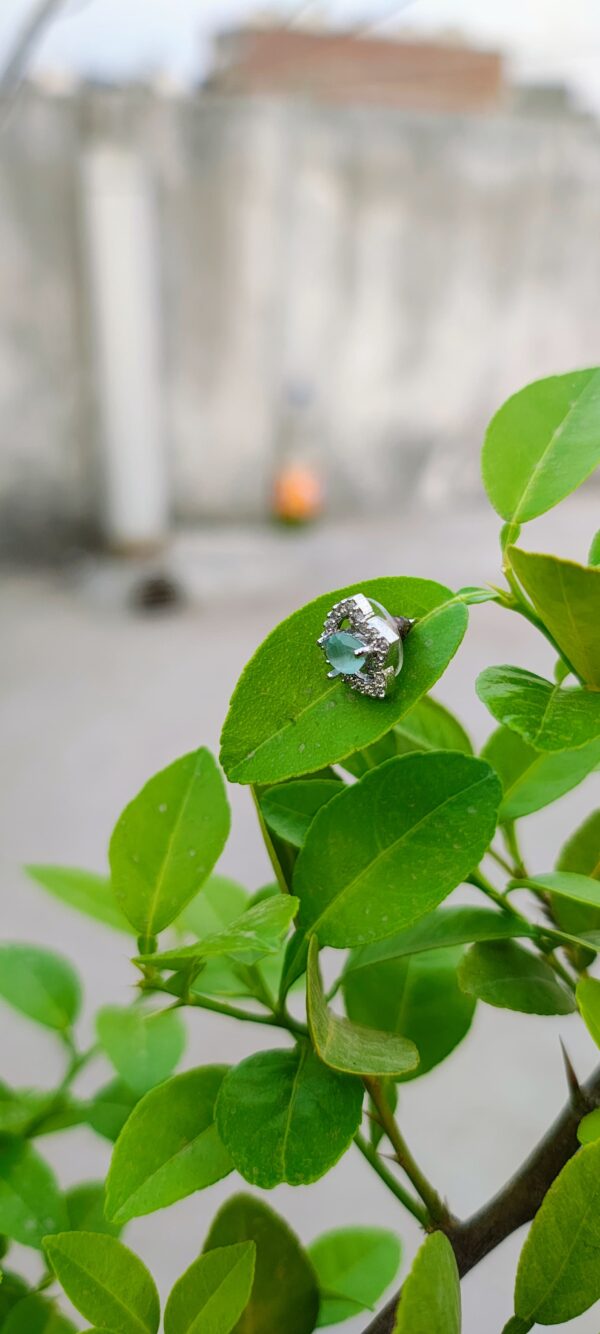 A pair of teardrop-shaped aqua stone stud earrings, encased in a sparkling crystal frame, placed on a white surface with a blurred natural background.