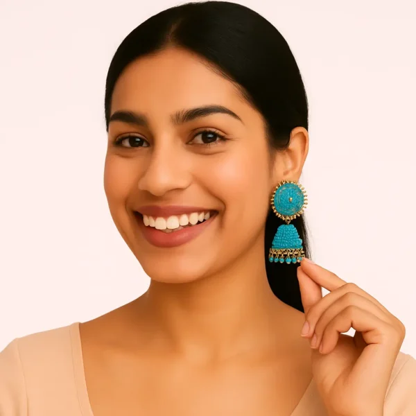 Smiling Indian woman with sleek hair wearing a beige top, showcasing a bold turquoise and gold jhumka earring.