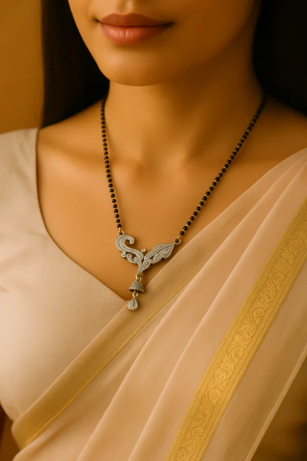 Close-up of a woman wearing a beige saree with a golden border, adorned with a leaf and jhumka design artificial mangalsutra featuring a black beaded chain and intricate silver-toned pendant design.