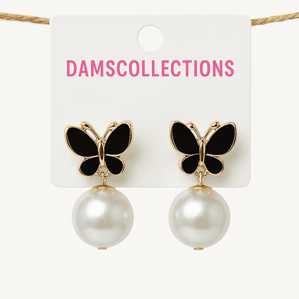 Two butterfly earrings with black enamel wings and gold-toned accents, each dangling a large white pearl, displayed on a white Dams Collections earring card suspended by a string.